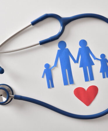Concept of family medicine with ostetoscope and paper cut of family and heart on a white table. Top view. Horizontal composition.