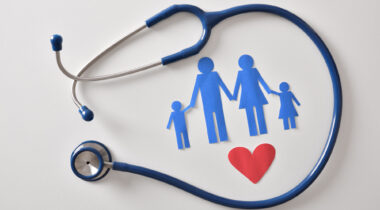 Concept of family medicine with ostetoscope and paper cut of family and heart on a white table. Top view. Horizontal composition.